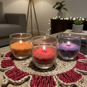 Three lit pearl sand wax candles in glass holders on a decorative mat in a cozy living room.